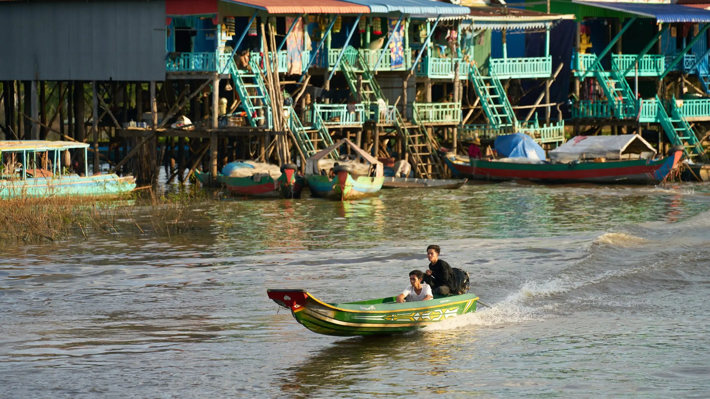 A boat passing stilted homes on the river at Kampong Khleang